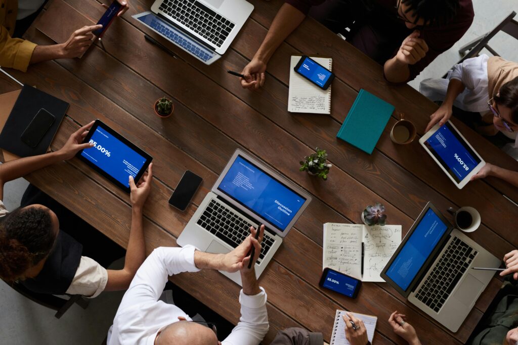 pexels-photo-3183183-3183183 Overhead view of a diverse team discussing around a wooden table, using technology.